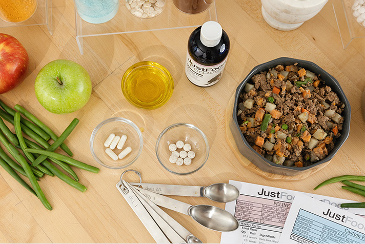 a custom just food for dogs recipe with cod, salmon, and sweet potato presented in a bowl with raw, fresh ingredients displayed around the bowl